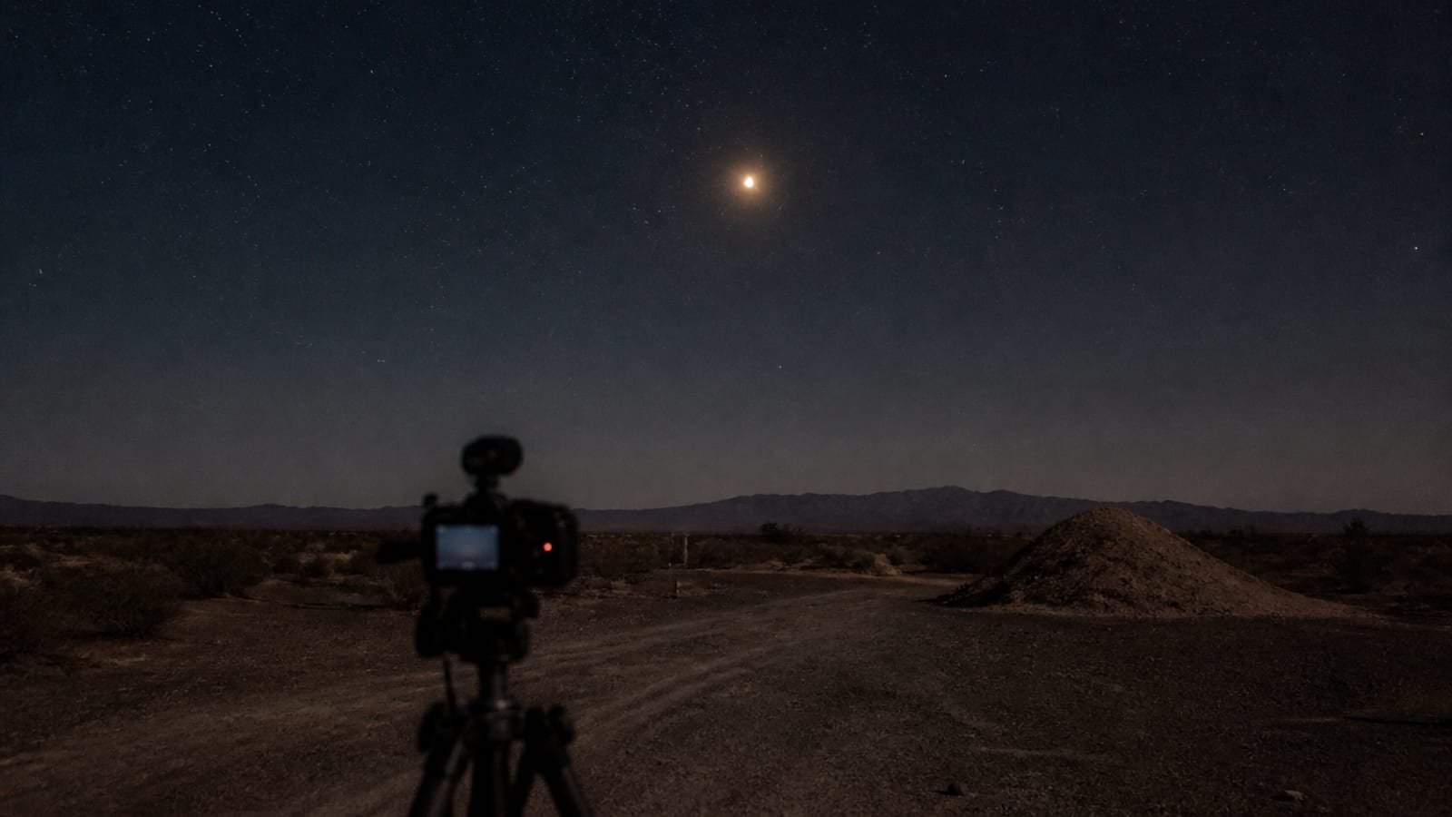 Night sky over a desert range with a distant light