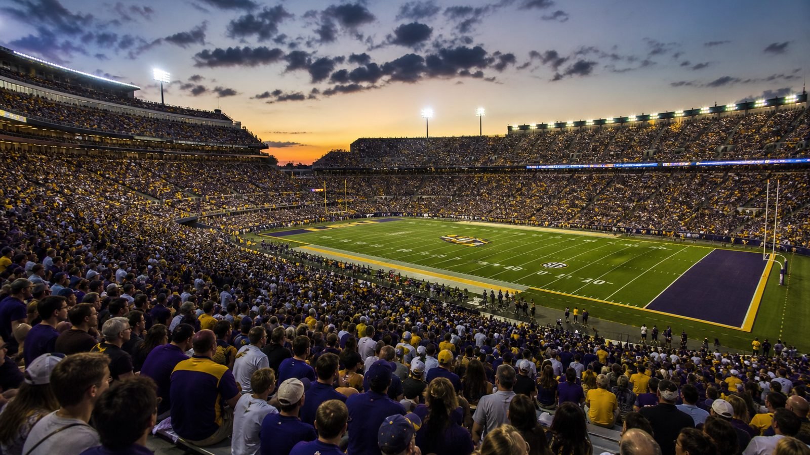 A packed college football stadium at dusk under the lights