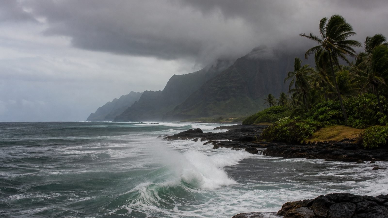 Dark Pacific surf pounding a Hawaiian volcanic coastline under a rain band