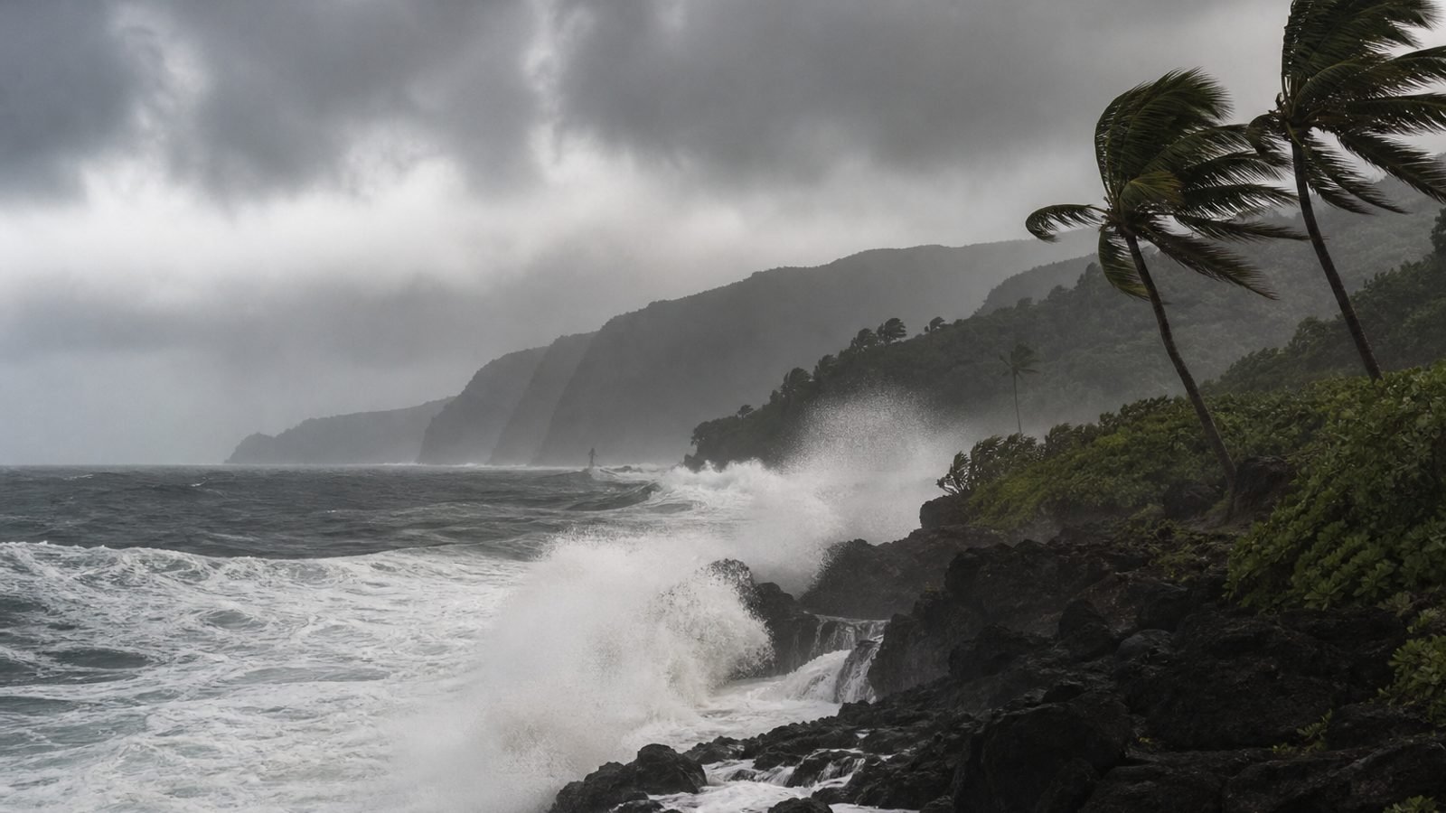 Dark Pacific surf pounding a Hawaiian volcanic coastline under rainbands