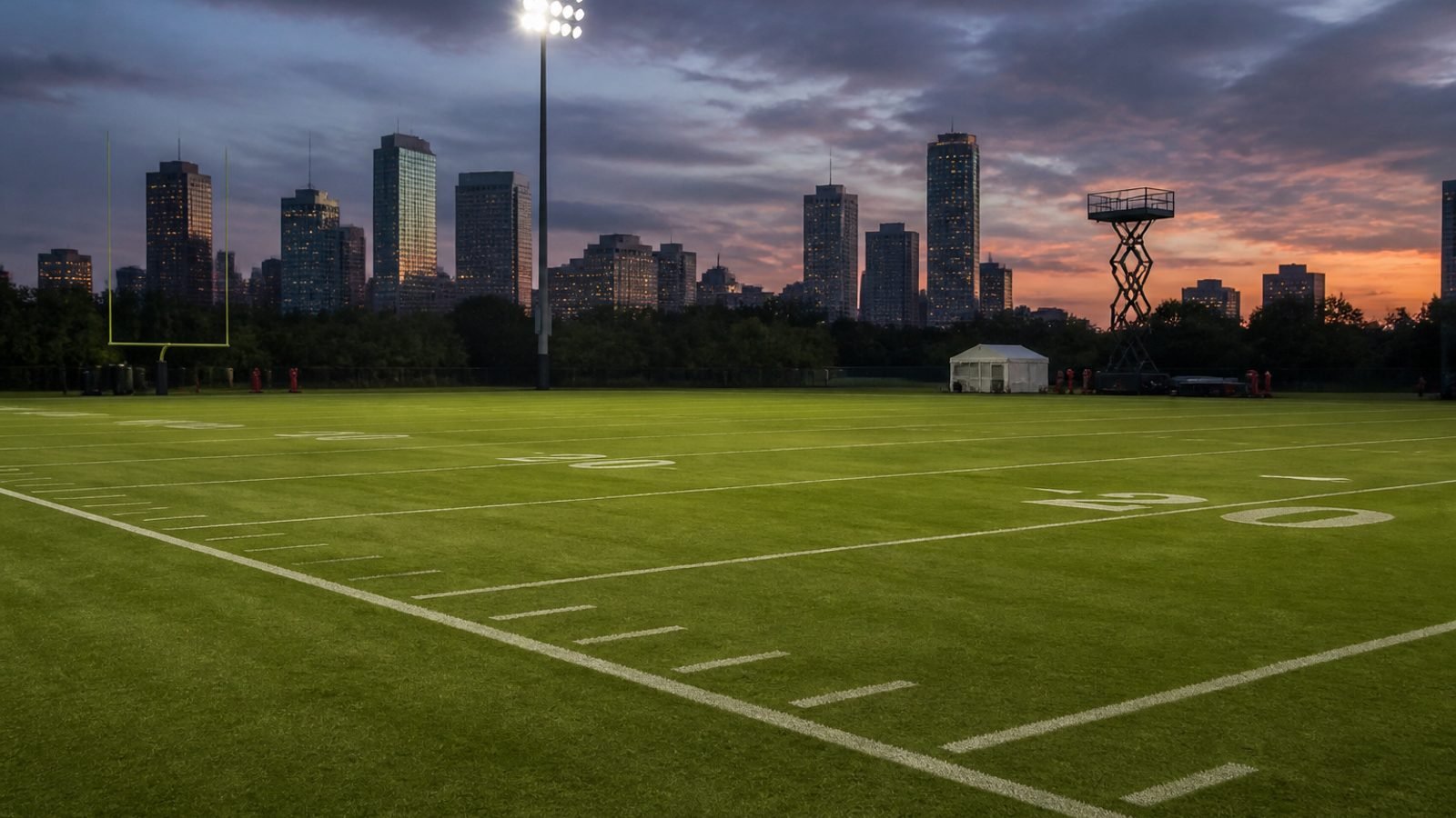 An empty football practice field under dusk stadium lights