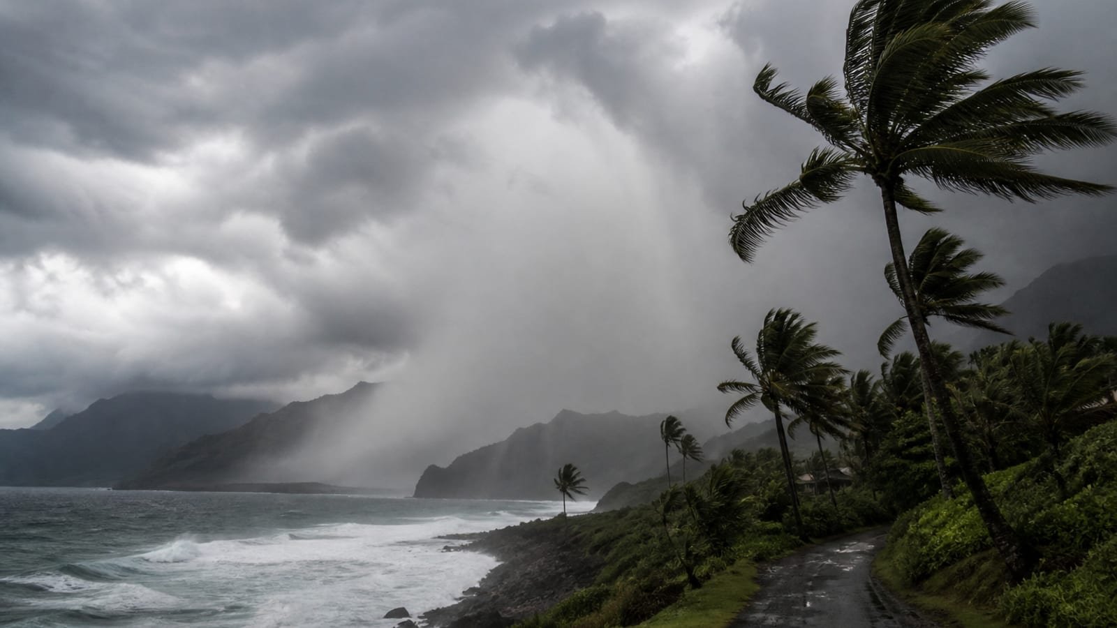 Dark Pacific surf slamming a Hawaiian rocky coast under a tropical rainband