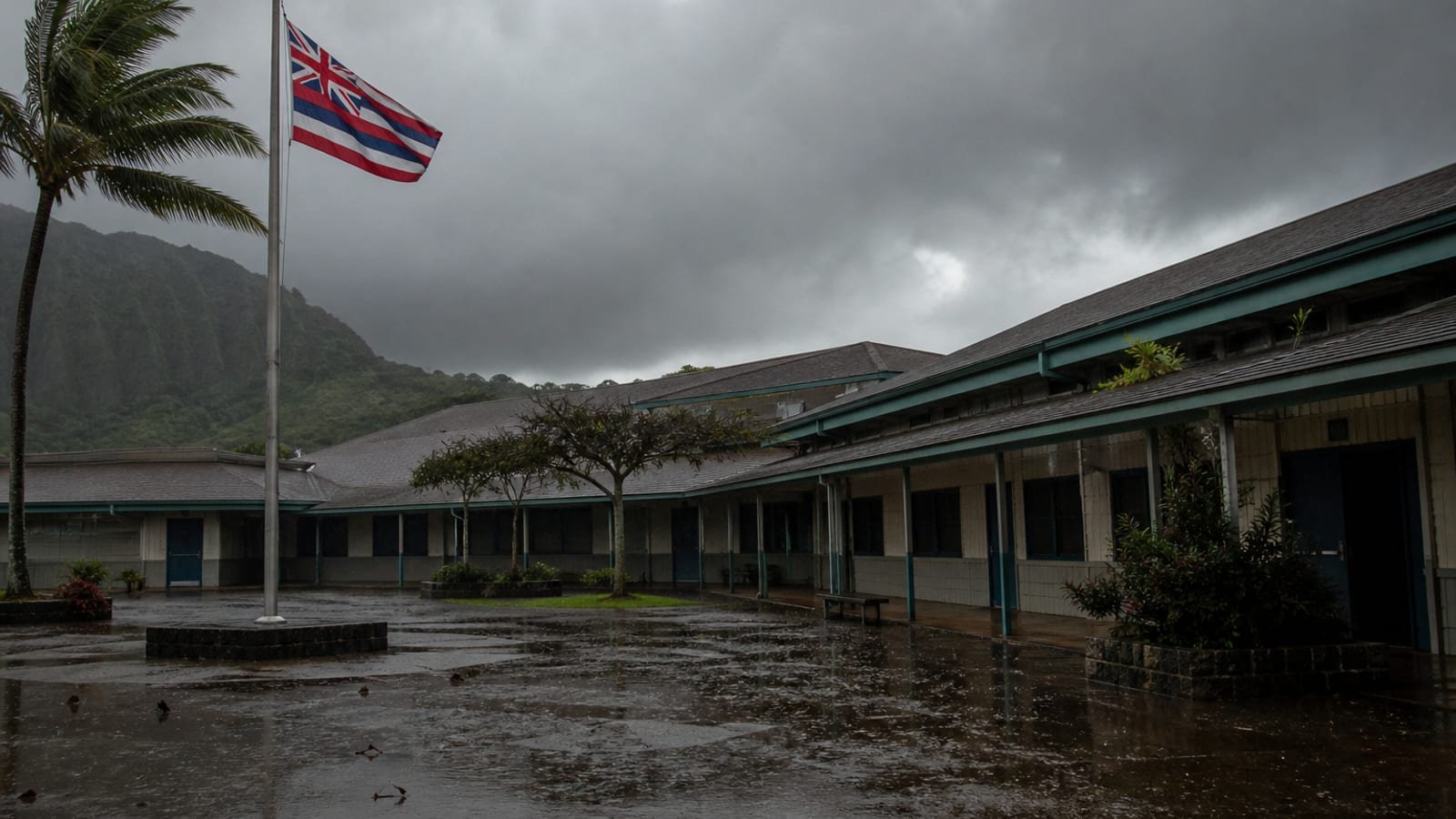 An empty Hawaiian school courtyard in heavy rain with classroom doors shut