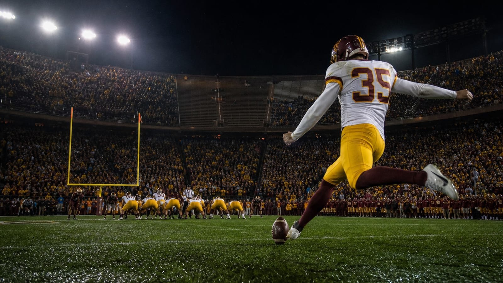 A college football kicker lining up a night field goal under stadium lights