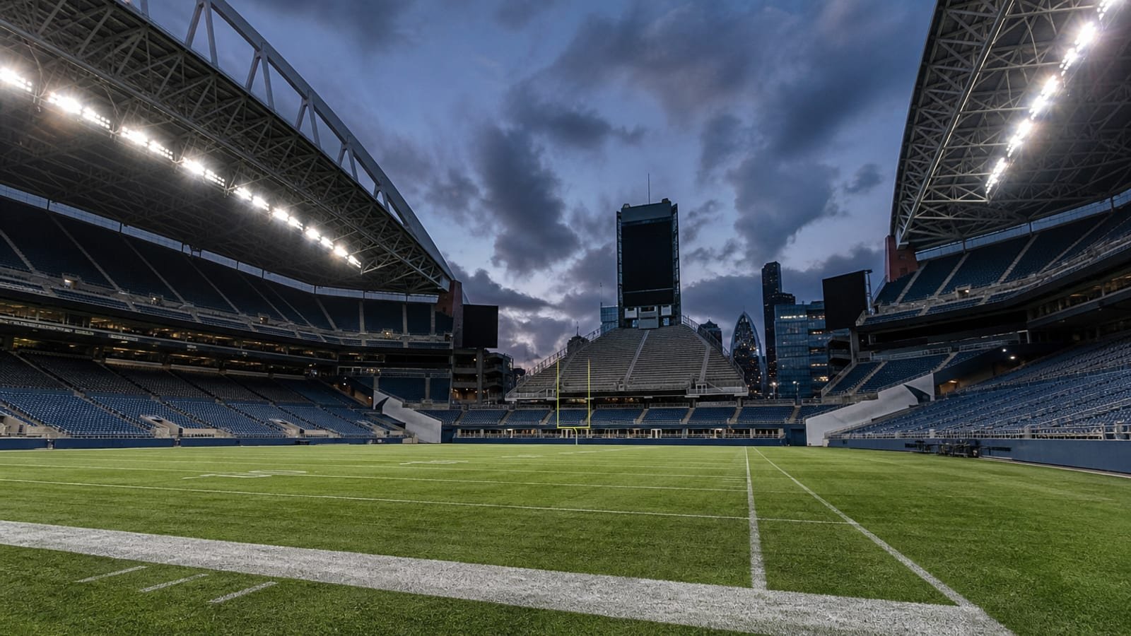 An NFL stadium at twilight with floodlights coming on over an empty field