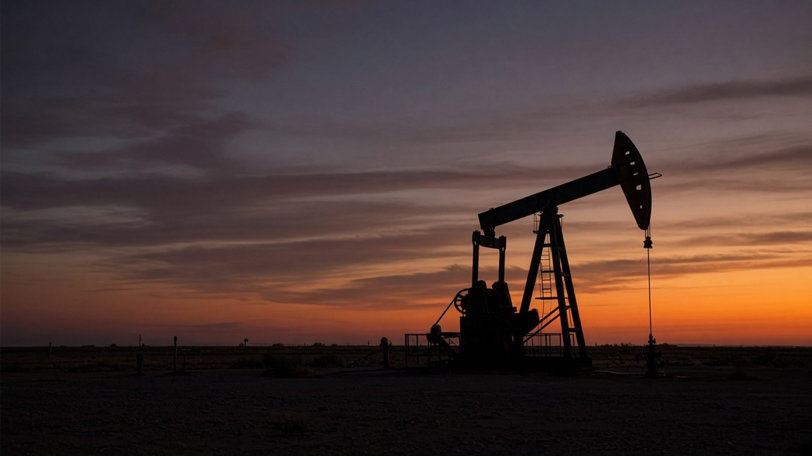 A pump jack silhouette on an empty oil field at dusk