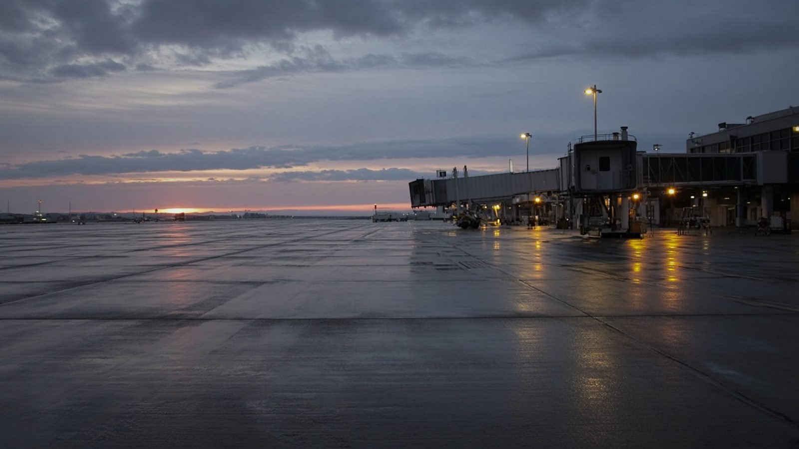 An empty airport tarmac at dawn with a distant jetway