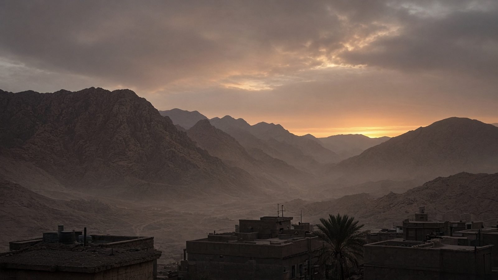 Rugged desert mountains at dusk above a dusty valley and rooftops