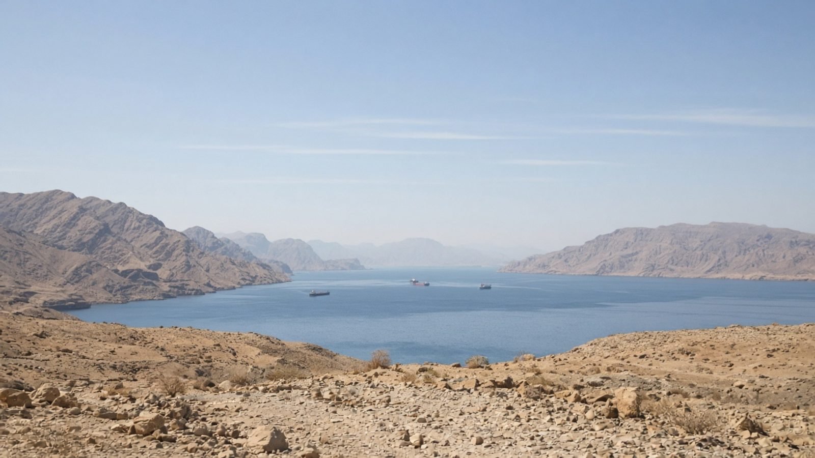 A narrow desert sea strait at midday with distant cargo ships