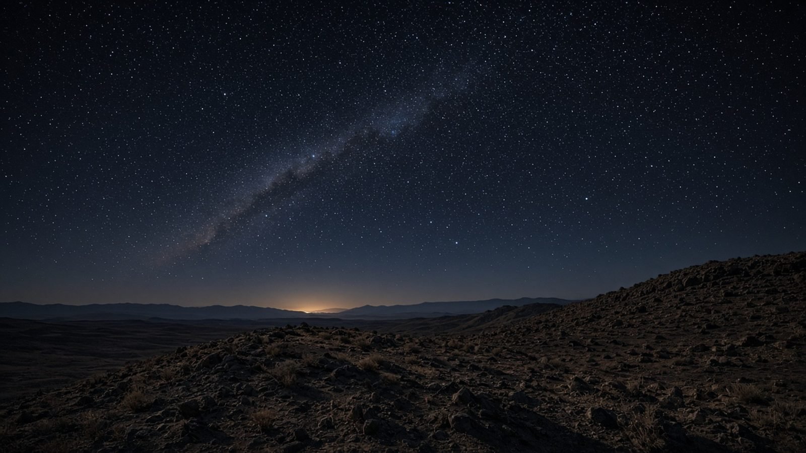 Night sky over a desert ridge with a faint distant light