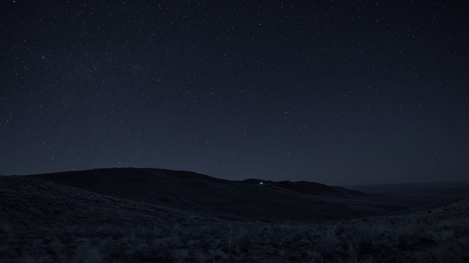 Night sky over a desert ridge with a faint distant light