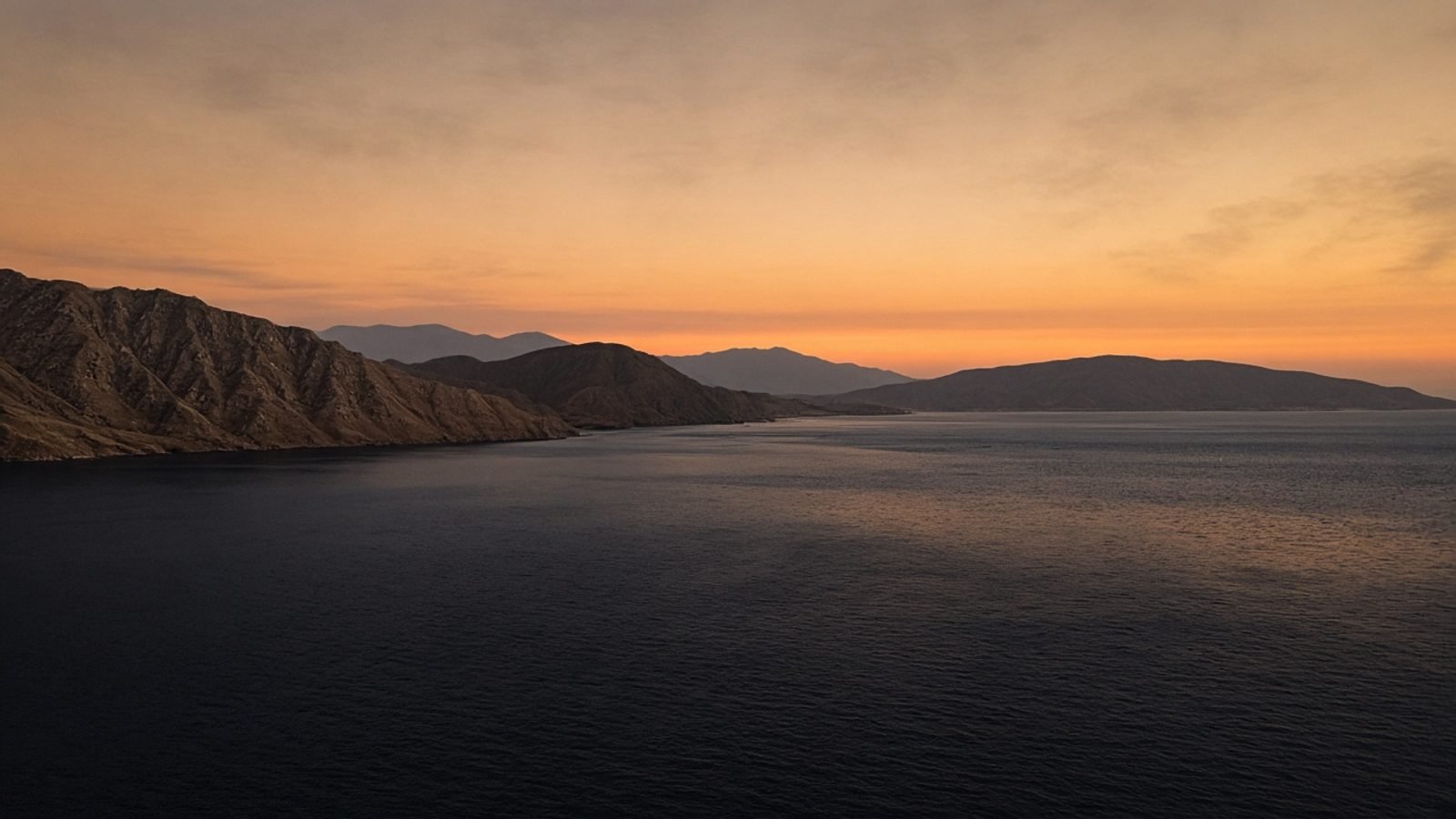 A tanker-free gulf strait at dusk with arid hills