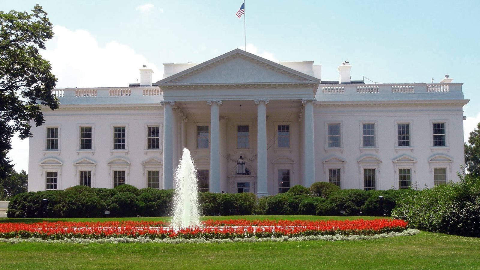 The north façade of the White House, including the portico, fountain, and flag. Photograph by Nishkid64, public domain.