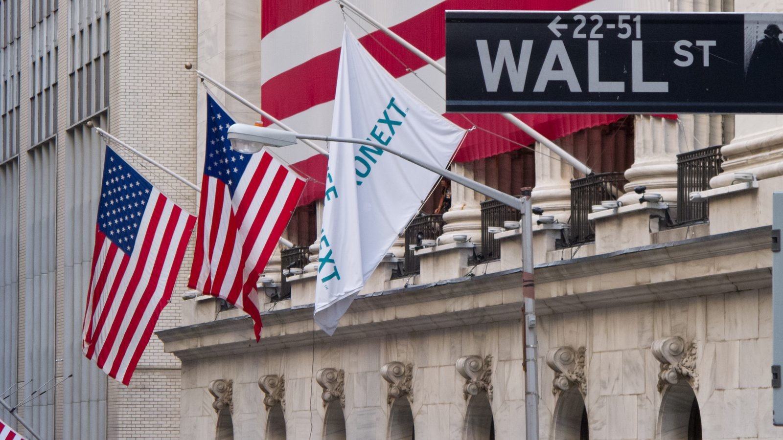 The New York Stock Exchange on Wall Street, with flags on the facade. Photograph by Carlos Delgado, CC BY-SA.