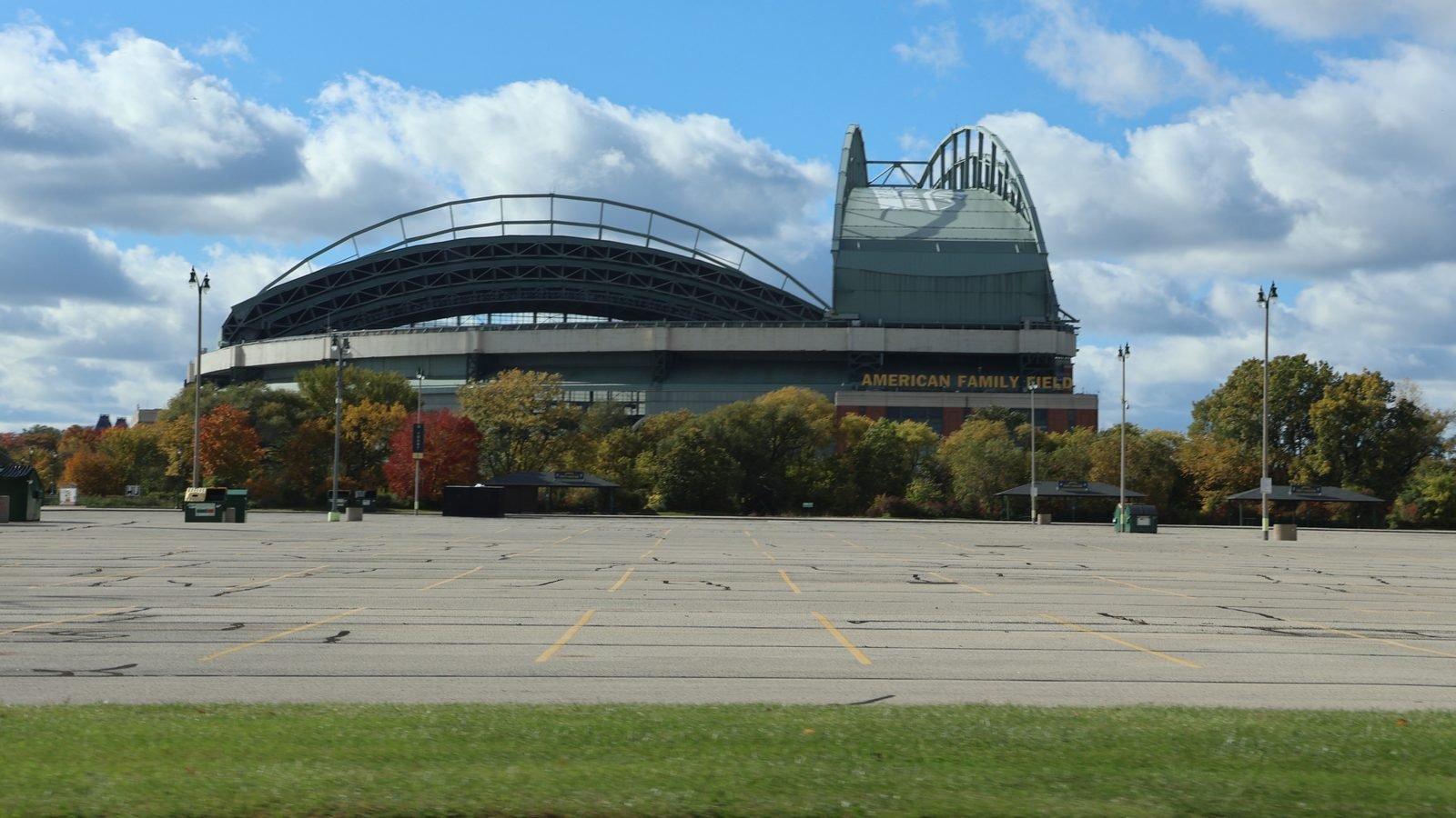 American Family Field in Milwaukee, seen from the parking lot, with autumn trees and the stadium name on the facade. Photograph by DiscoA340, CC BY-SA.