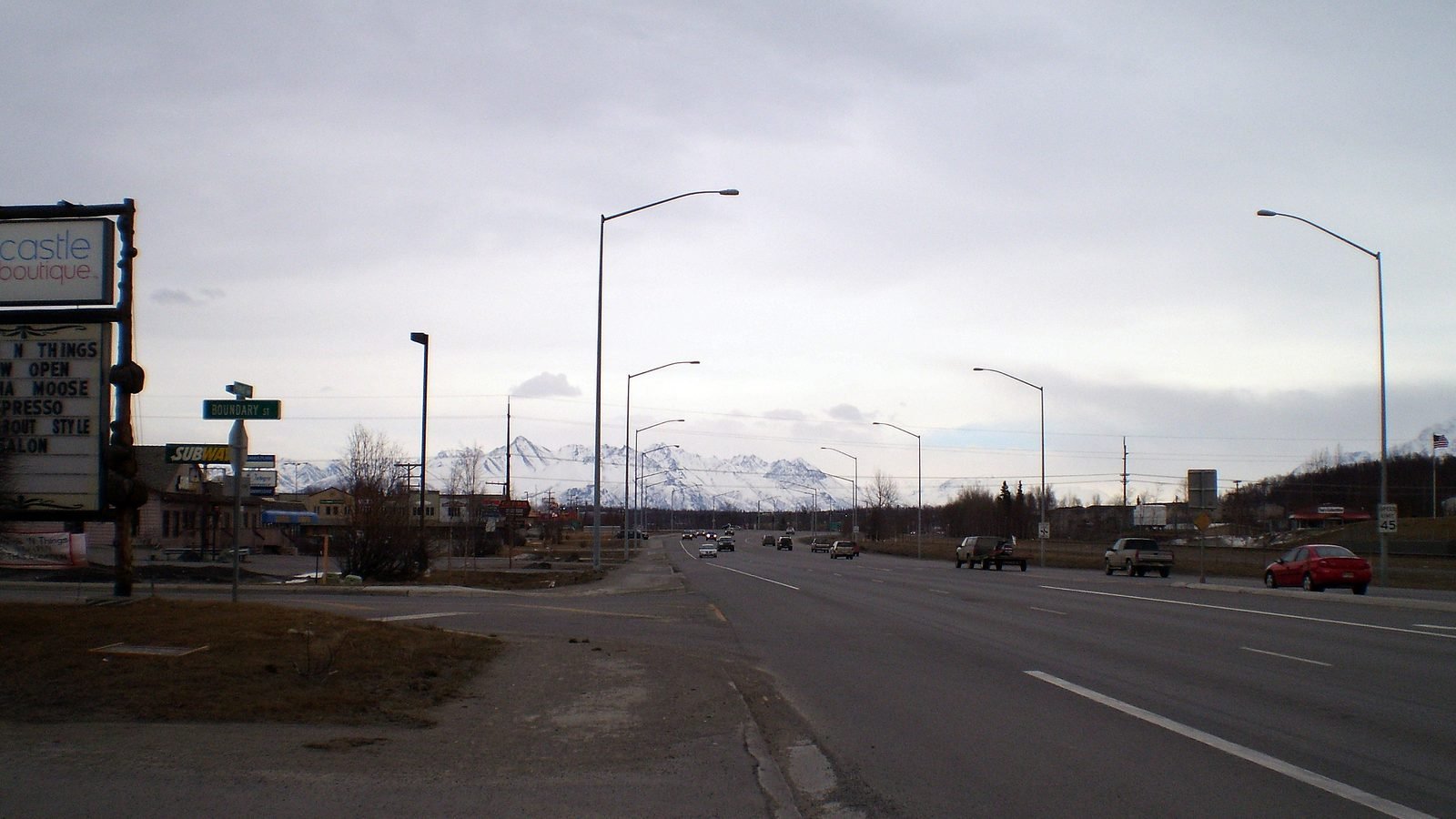The Parks Highway in Wasilla, Alaska, with commercial signs and snow-capped mountains. Photograph by James Brooks, CC BY.